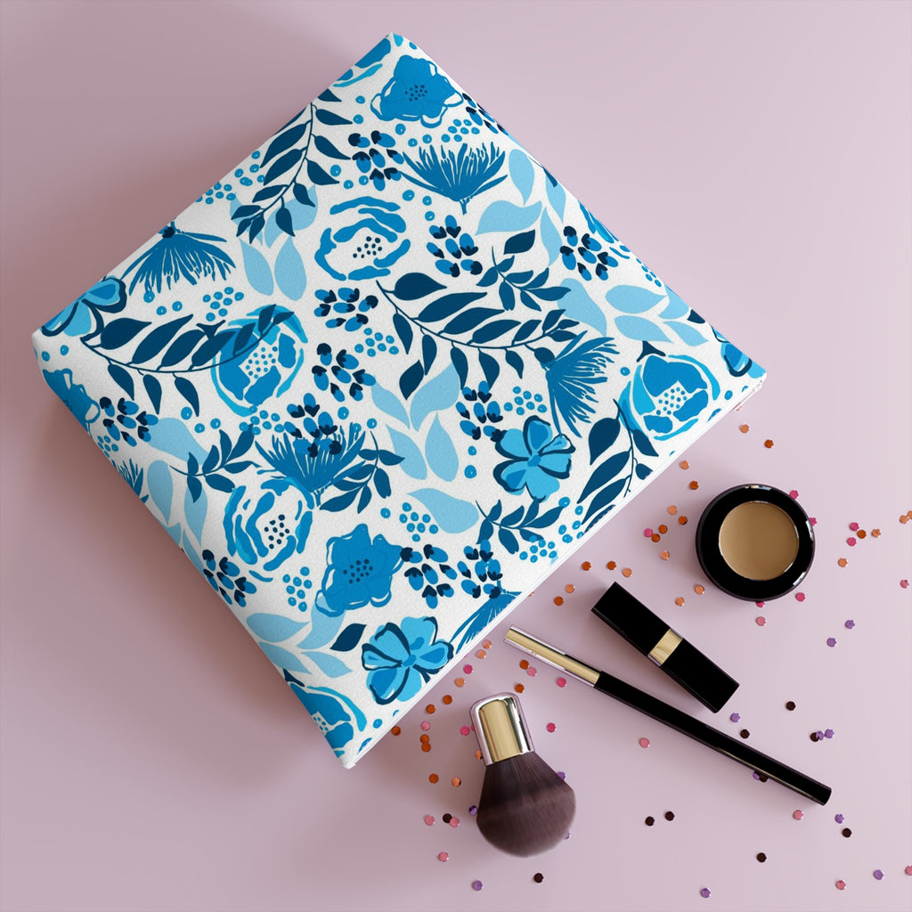 Cosmetic bag with white zipper and a blue floral design with flowers and leafy stems on a white background and laying on it's side with make up contents and confetti coming out of it.