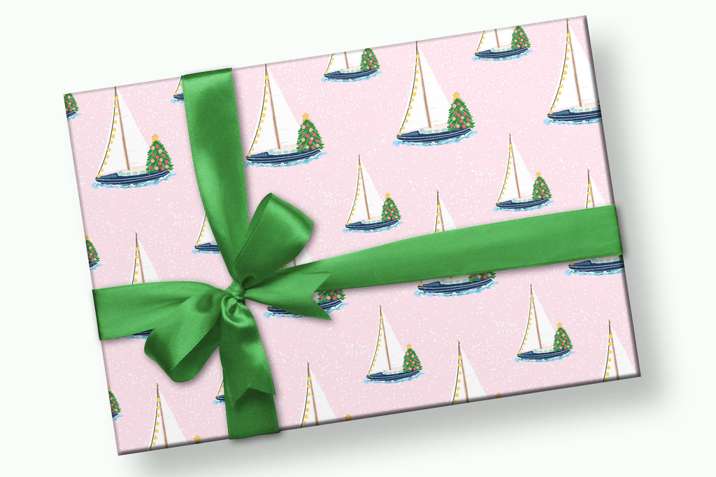 Gift with wrapping paper of Sailboats with lights and christmas tree on it on a light pink background and a green bow.