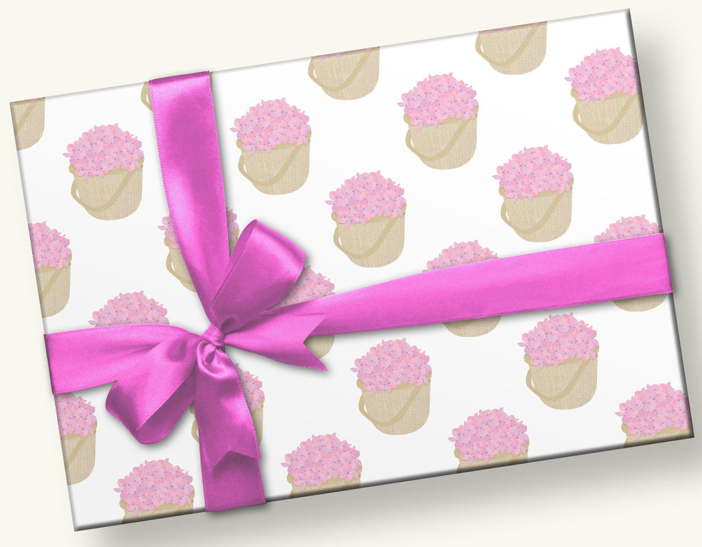 This is a photo of a gift with hot pink ribbon and bow. The gift wrap is an arrangement of the same motif - pink colored hydrangeas in a Nantucket basket and they are scattered on a white background.